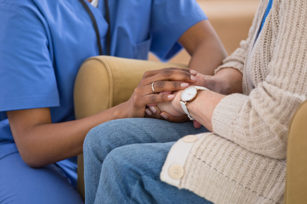 Part of female home caregiver supporting senior woman in her house, holding hands. Close up of hands, unrecognisable people. in a care home