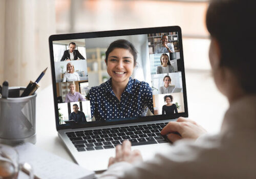 Woman sit at desk looking at computer screen where collage of diverse people webcam view. Indian ethnicity young woman lead video call distant chat